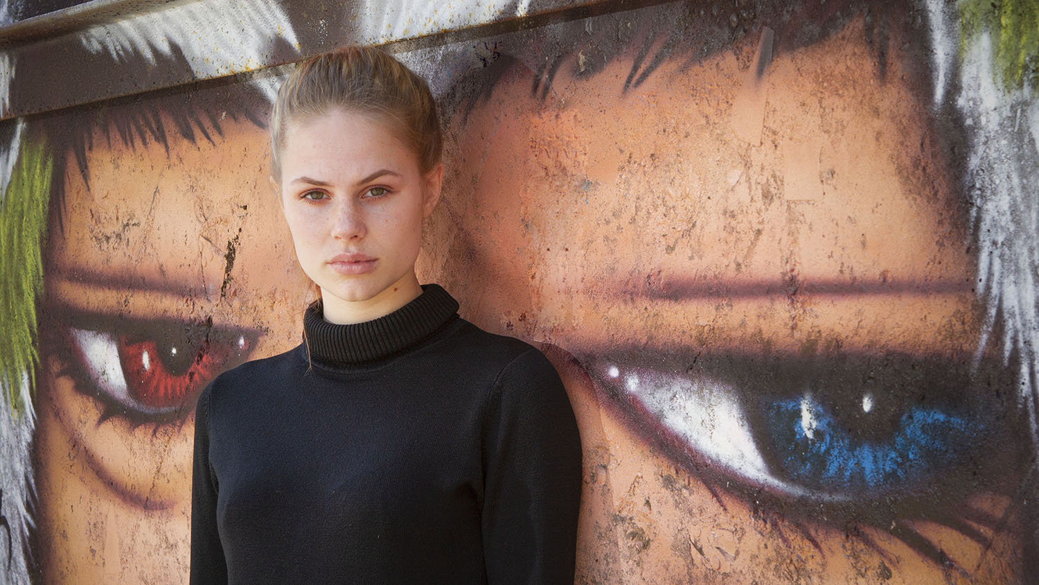 Een model in een zwarte trui voor een beschilderde muur