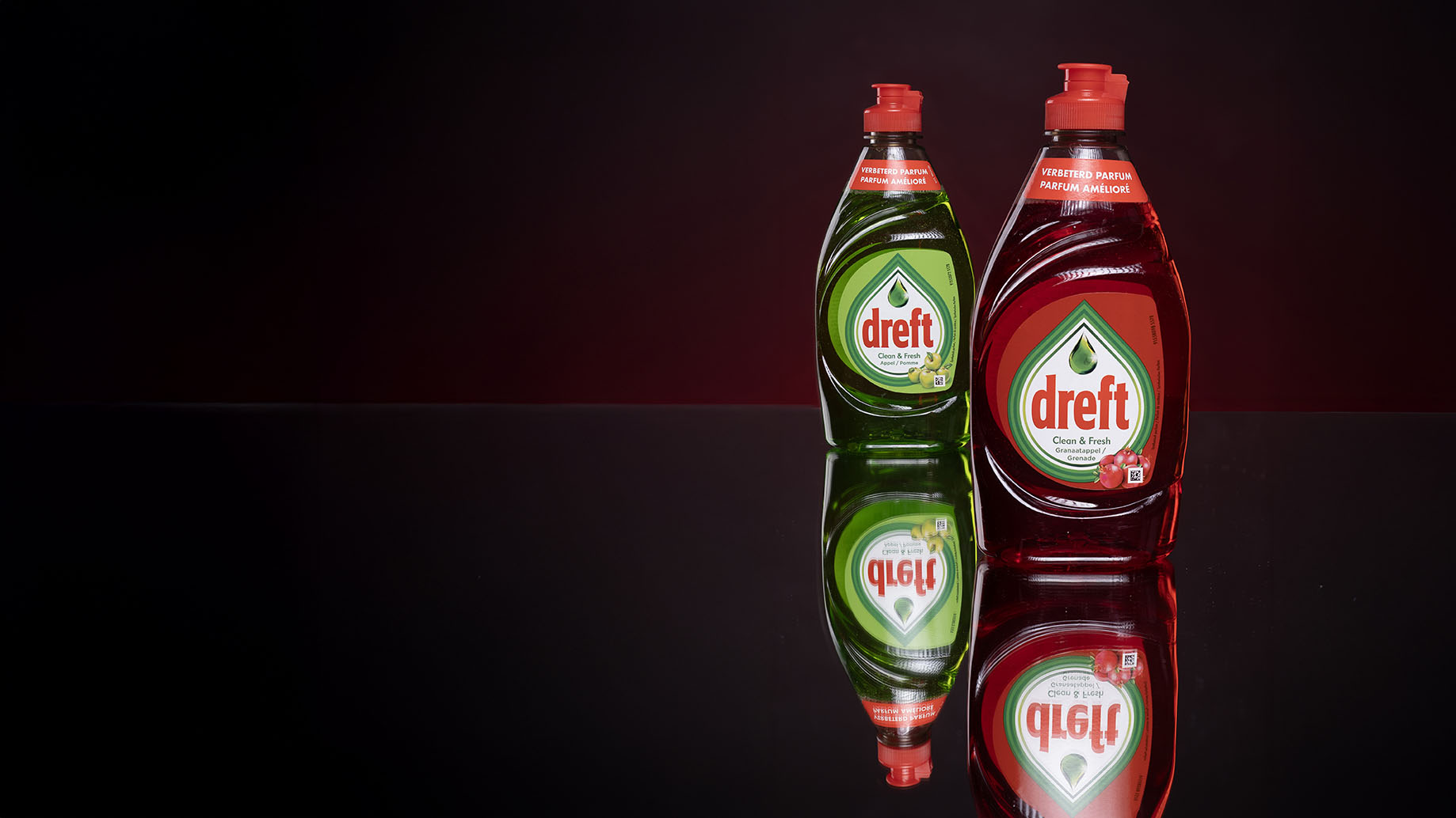 Een groene en een rode fles Dreft met hun weerspiegeling op een donkere ondergrond